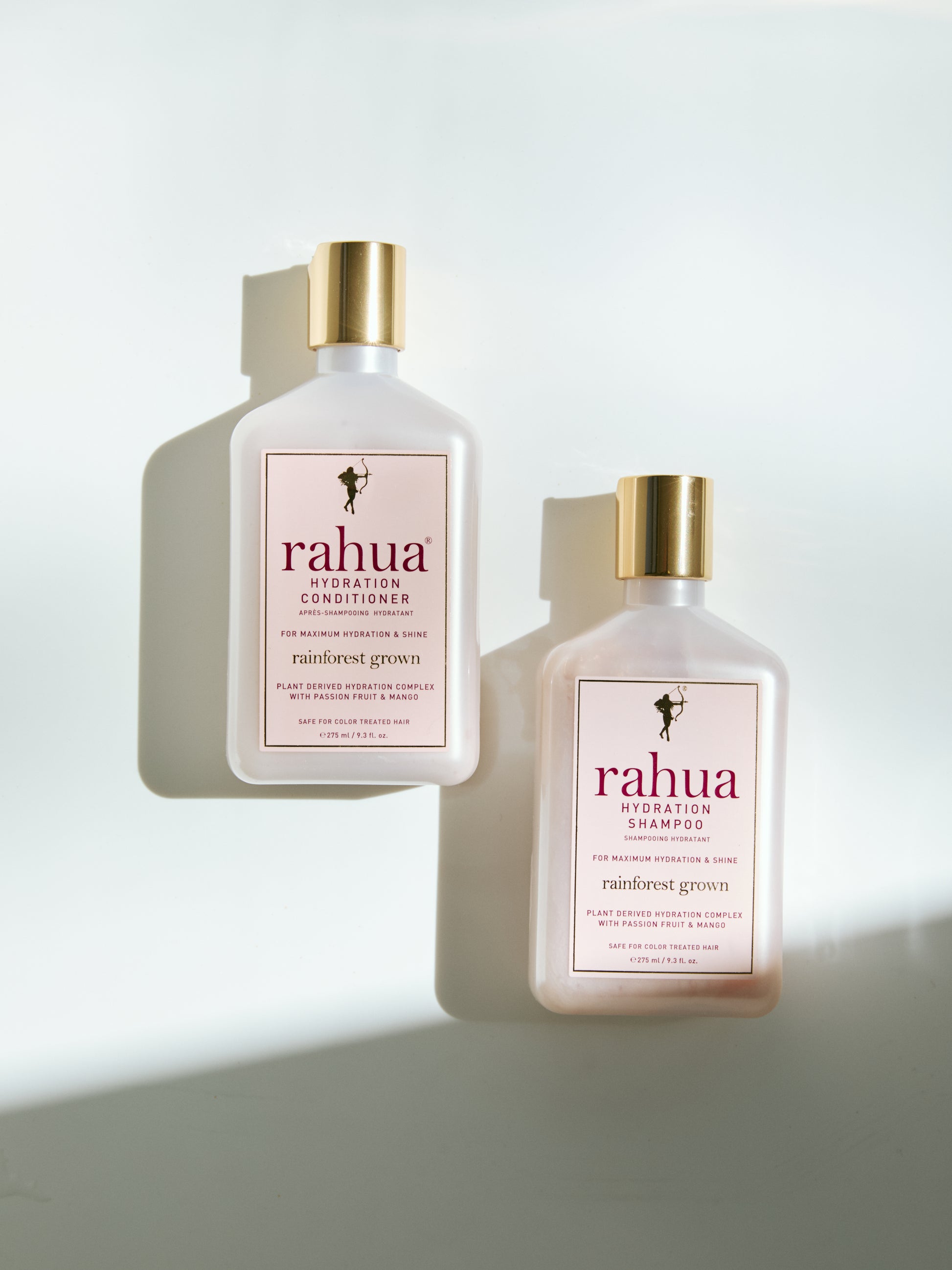 two bottles of rahua hydration conditioner and shampoo pink plastic bottles with gold caps set on a plain white background|variant:16-oz