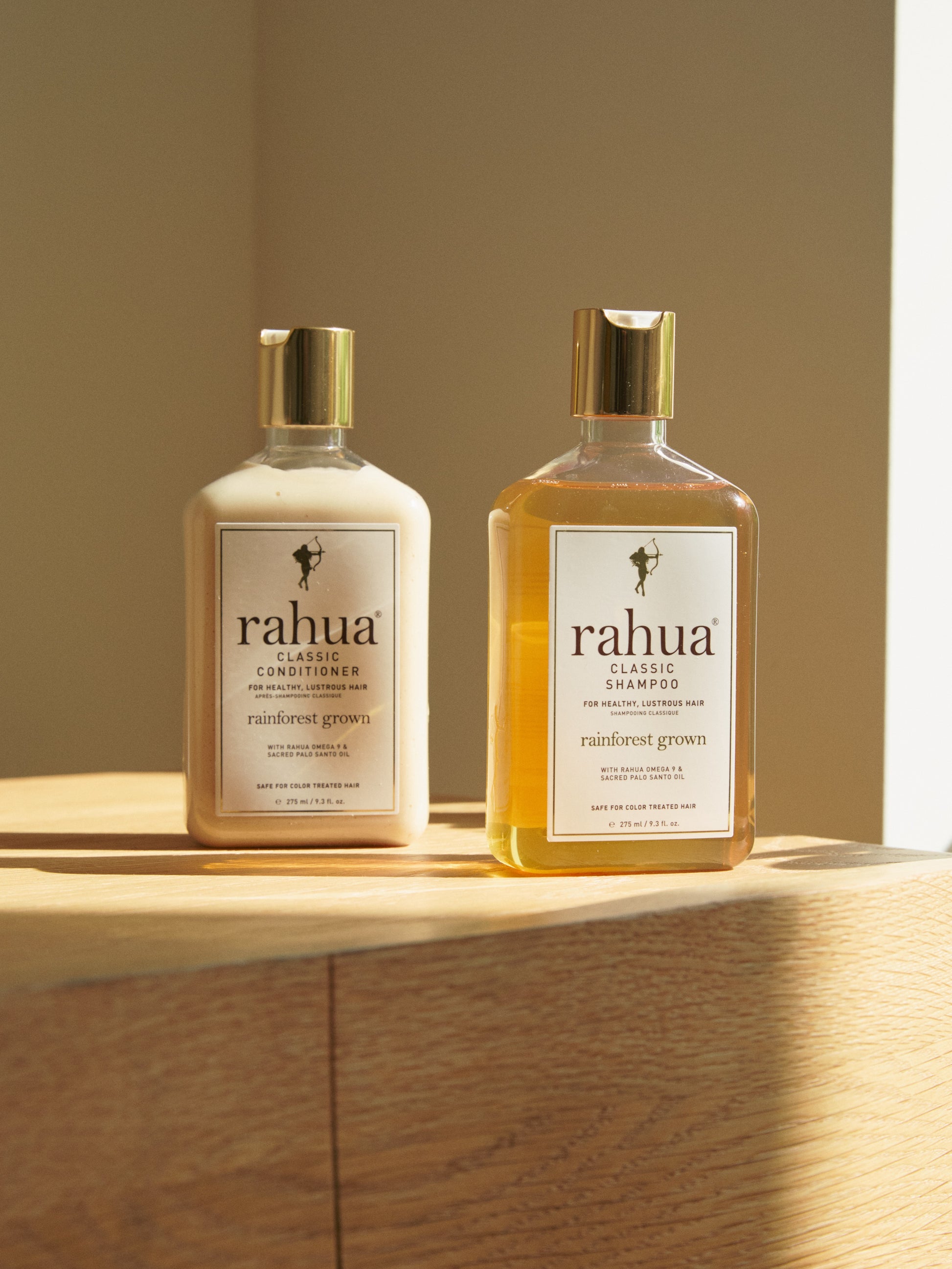 two bottles of rahua classic shampoo and classic conditioner on top of a wooden table on a plain beige background|variant:16-oz