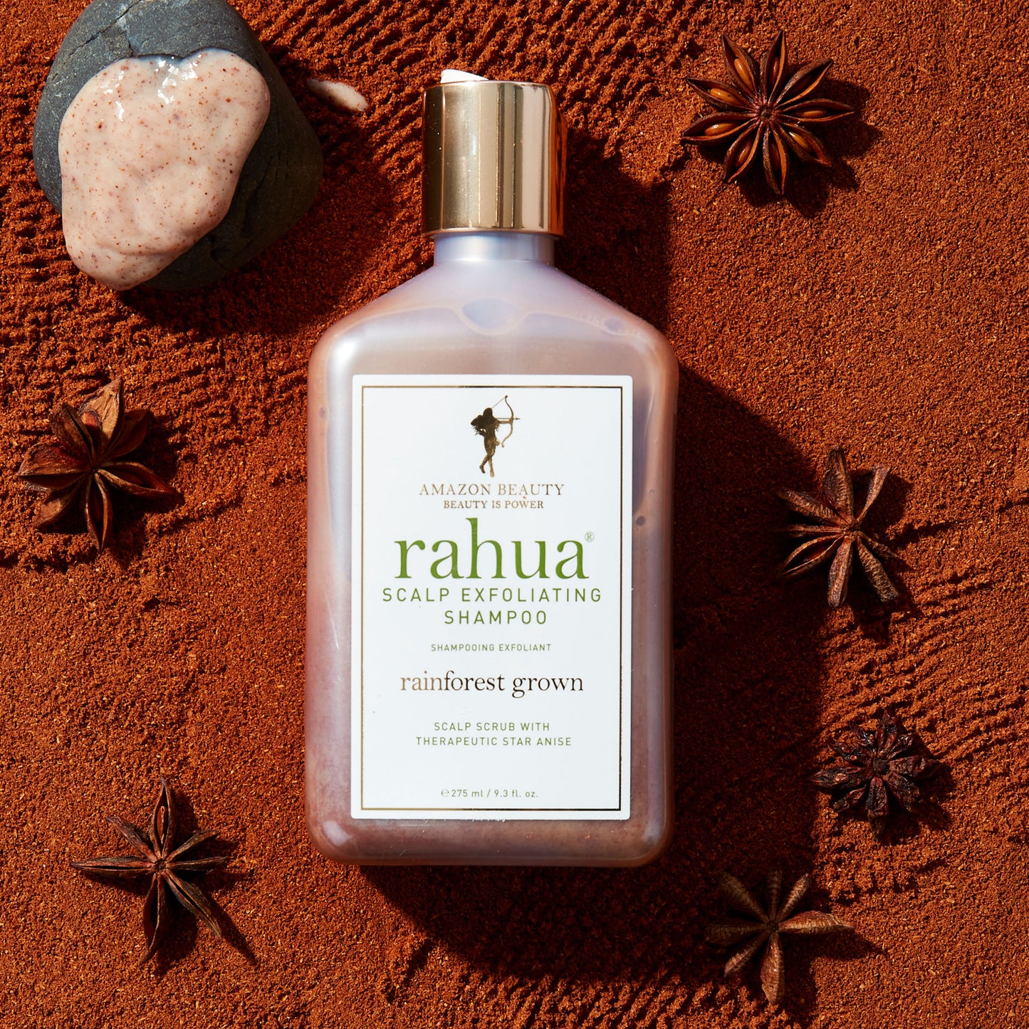 bottle with gold cap with white label and green letter rahua scalp exfoliating shampoo on a background of crushed and whole star anise with comb through textures|variant:93-oz