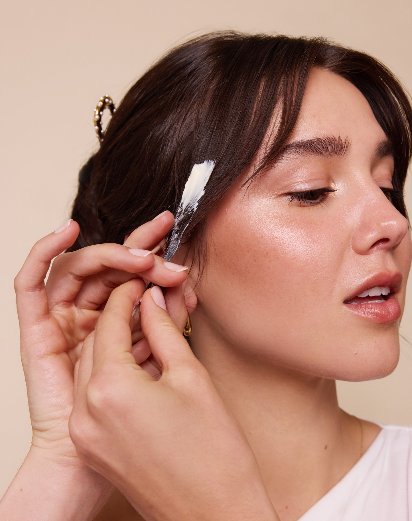 Woman applying cream to her ear with a small brush against a beige background