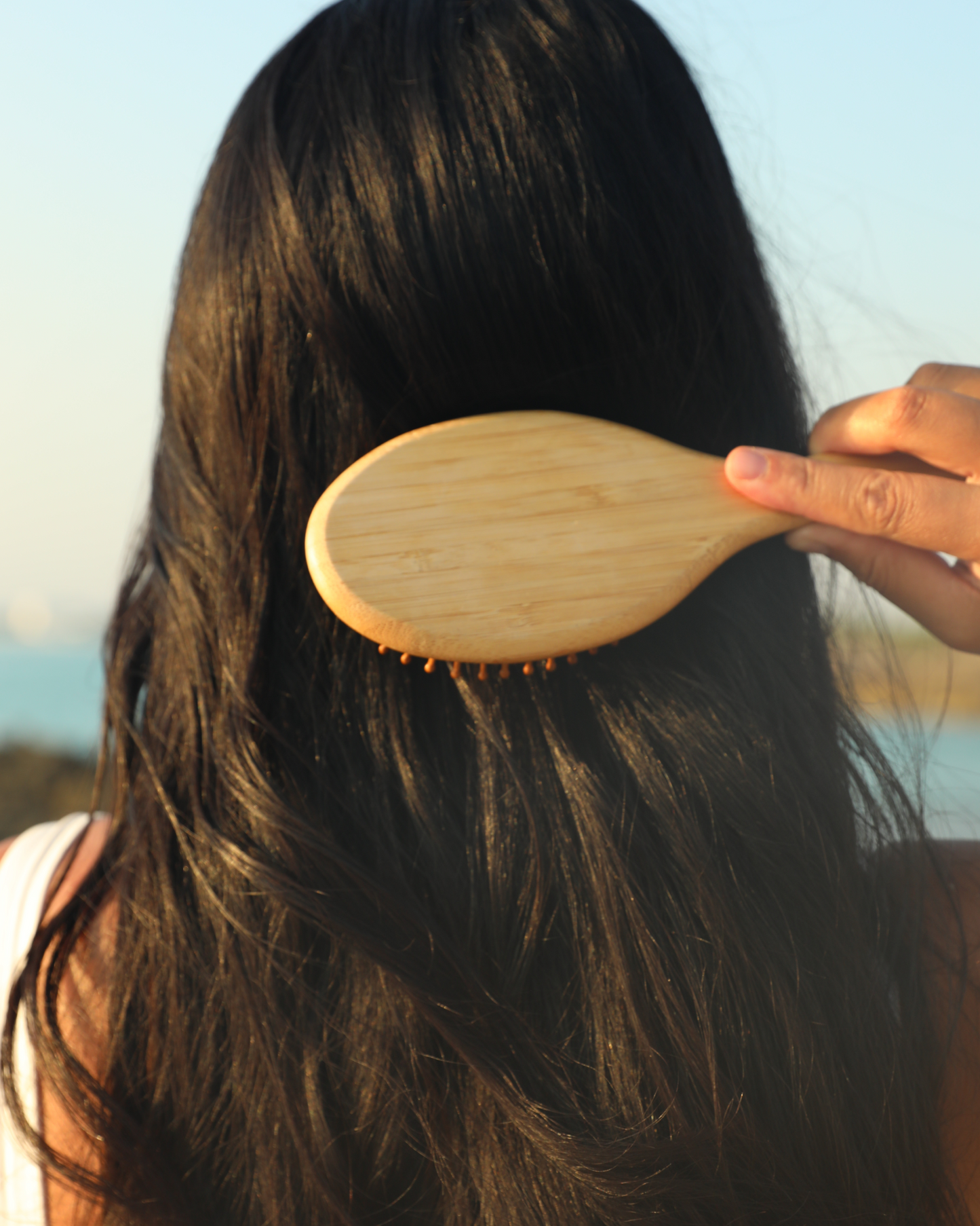 Person using a wooden hairbrush on their hair with a blurred natural background|variant:93-oz,16-oz,18-oz