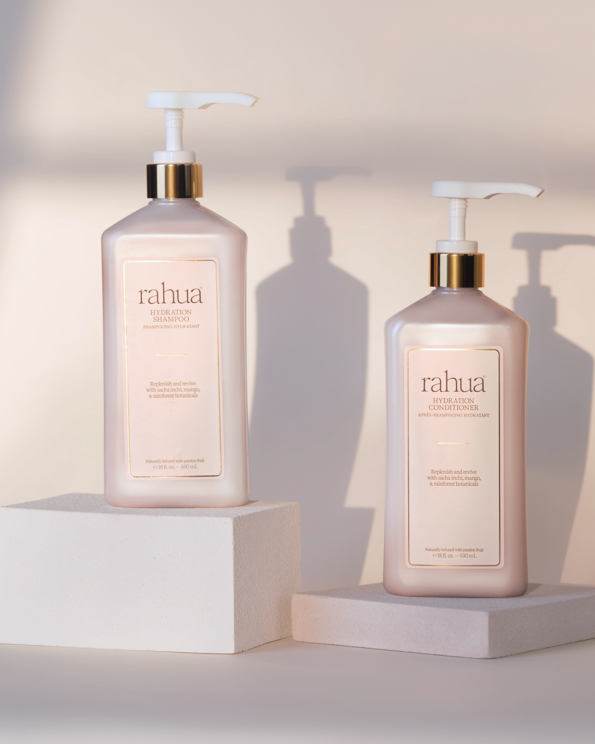 Two Rahua hair care products on white stands with a neutral background|variant:18-oz