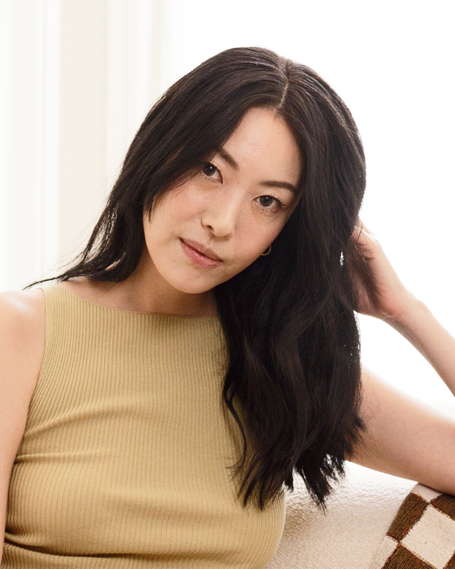 Woman with long dark hair wearing a beige sleeveless top against a neutral background|variant:93-oz,16-oz,18-oz