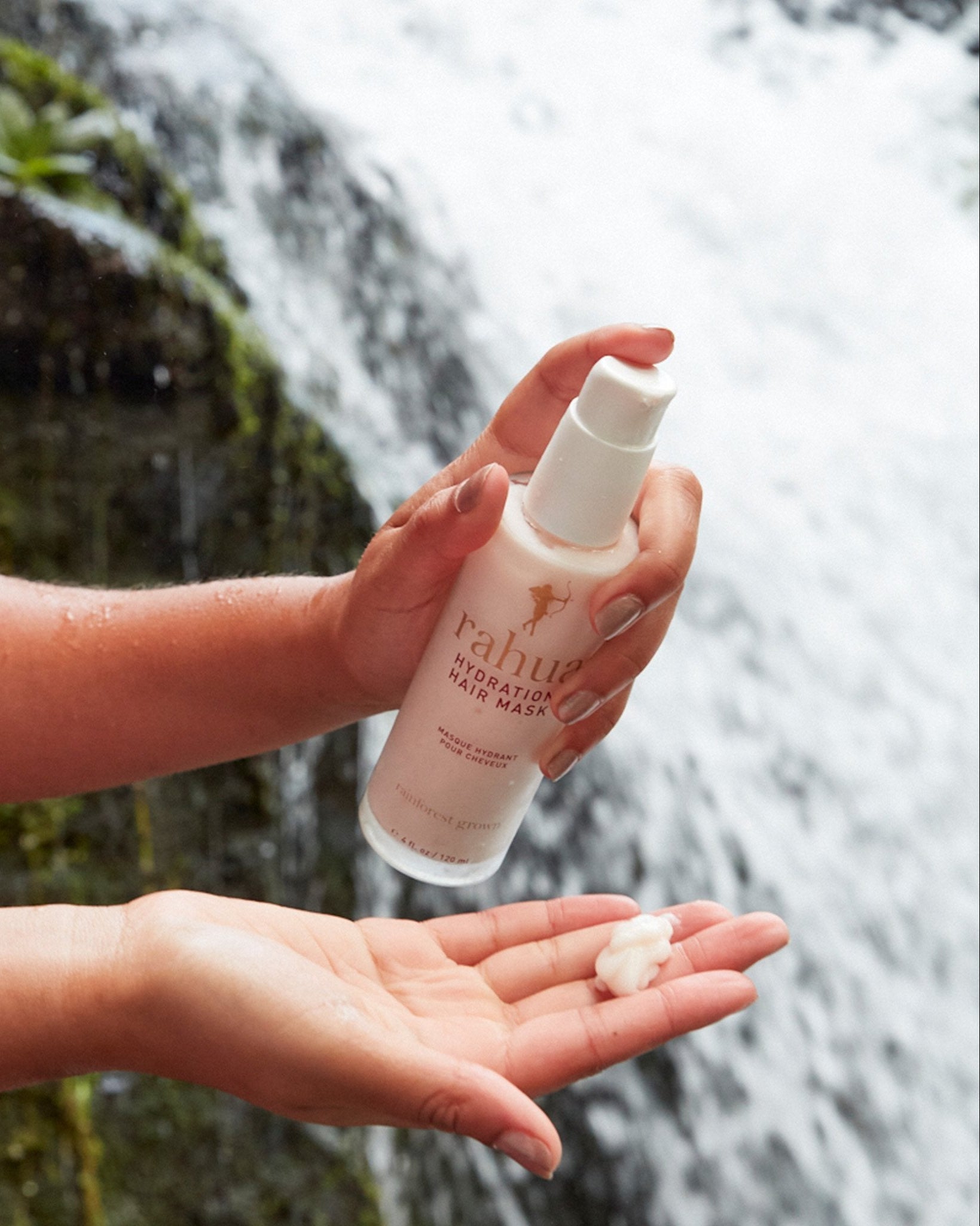 model dispensing product onto their hand glass bottle of rahua hydration hair mask with a background of a waterfall|variant:4-oz