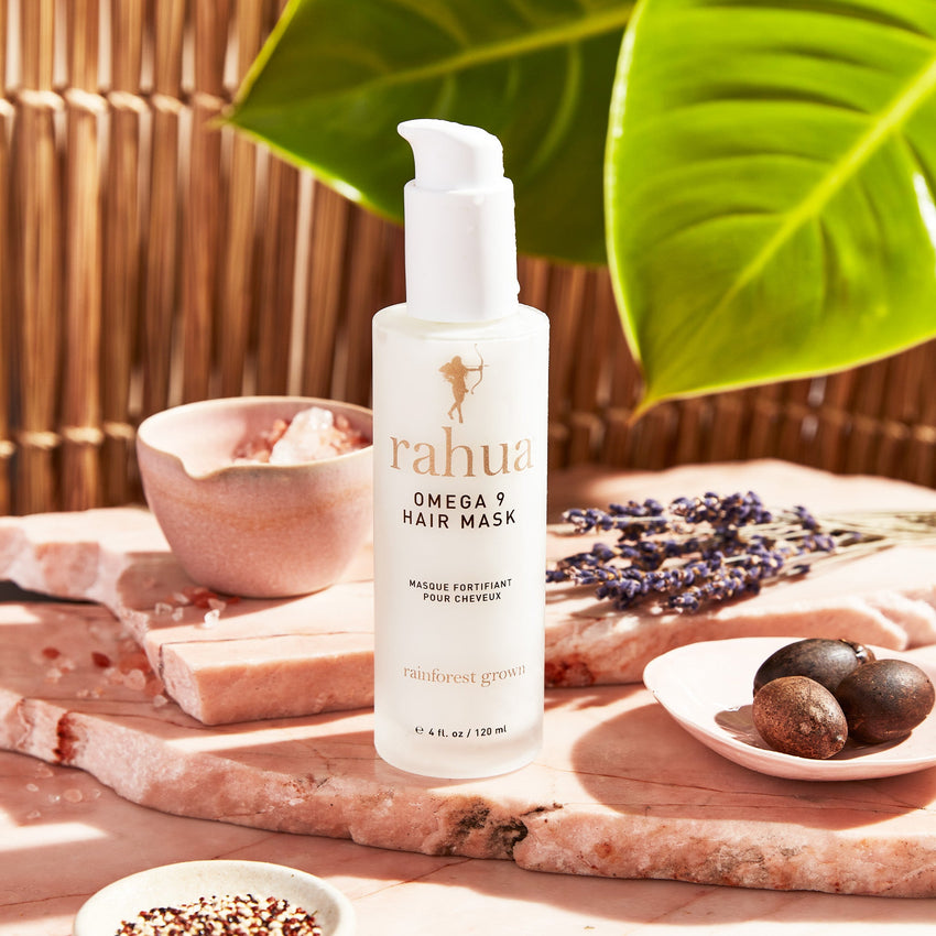 bottle of white product with gold and brown text rahua omega 9 hair mask on a stone slab with quinoa and leaves|variant:4-oz