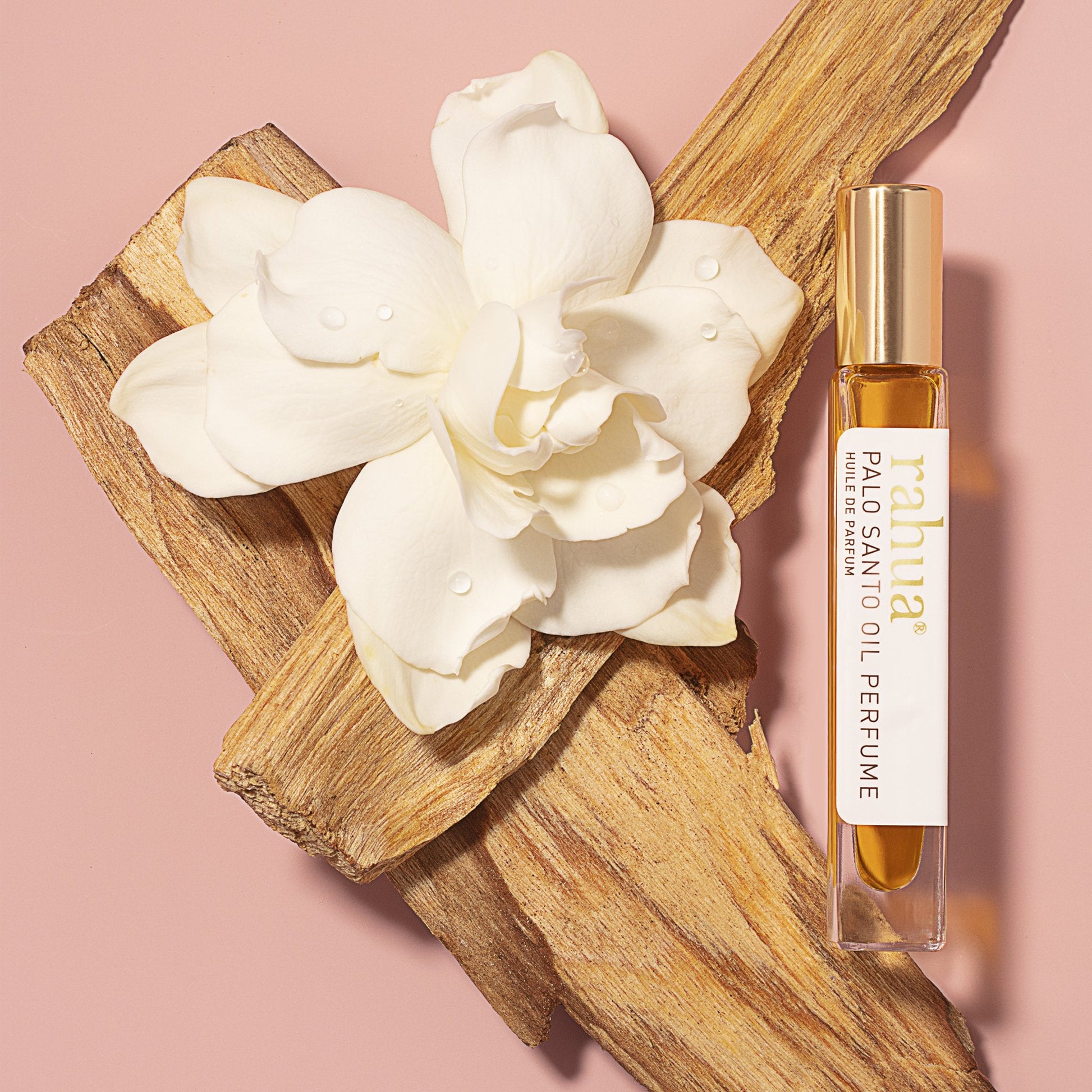 Rahua Palo Santo Oil perfume placed in between palo santo sticks and white gardenia flower